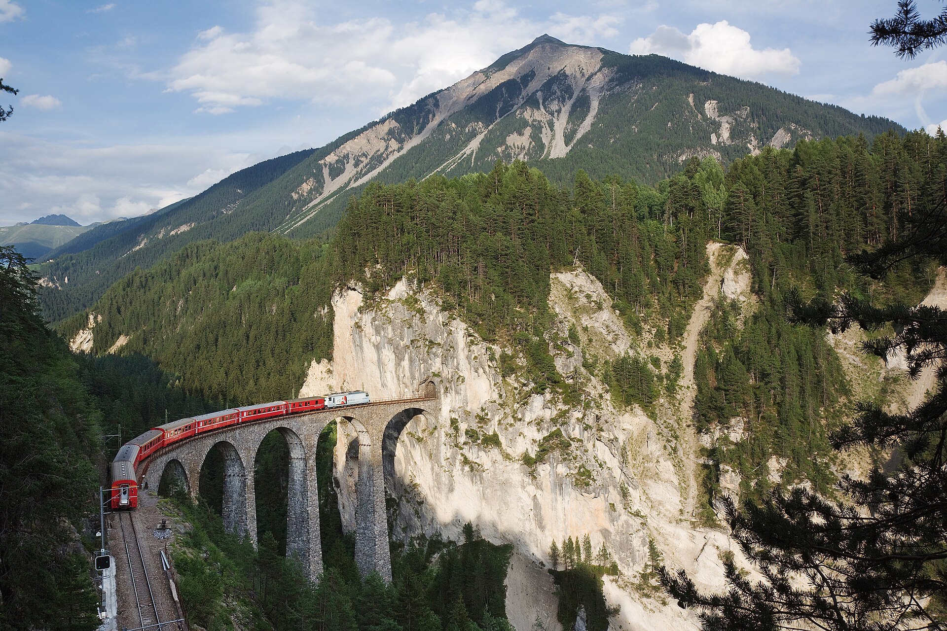 A red Rhaetian Railway train crossing the curved Landwasser Viaduct on the Albula line.