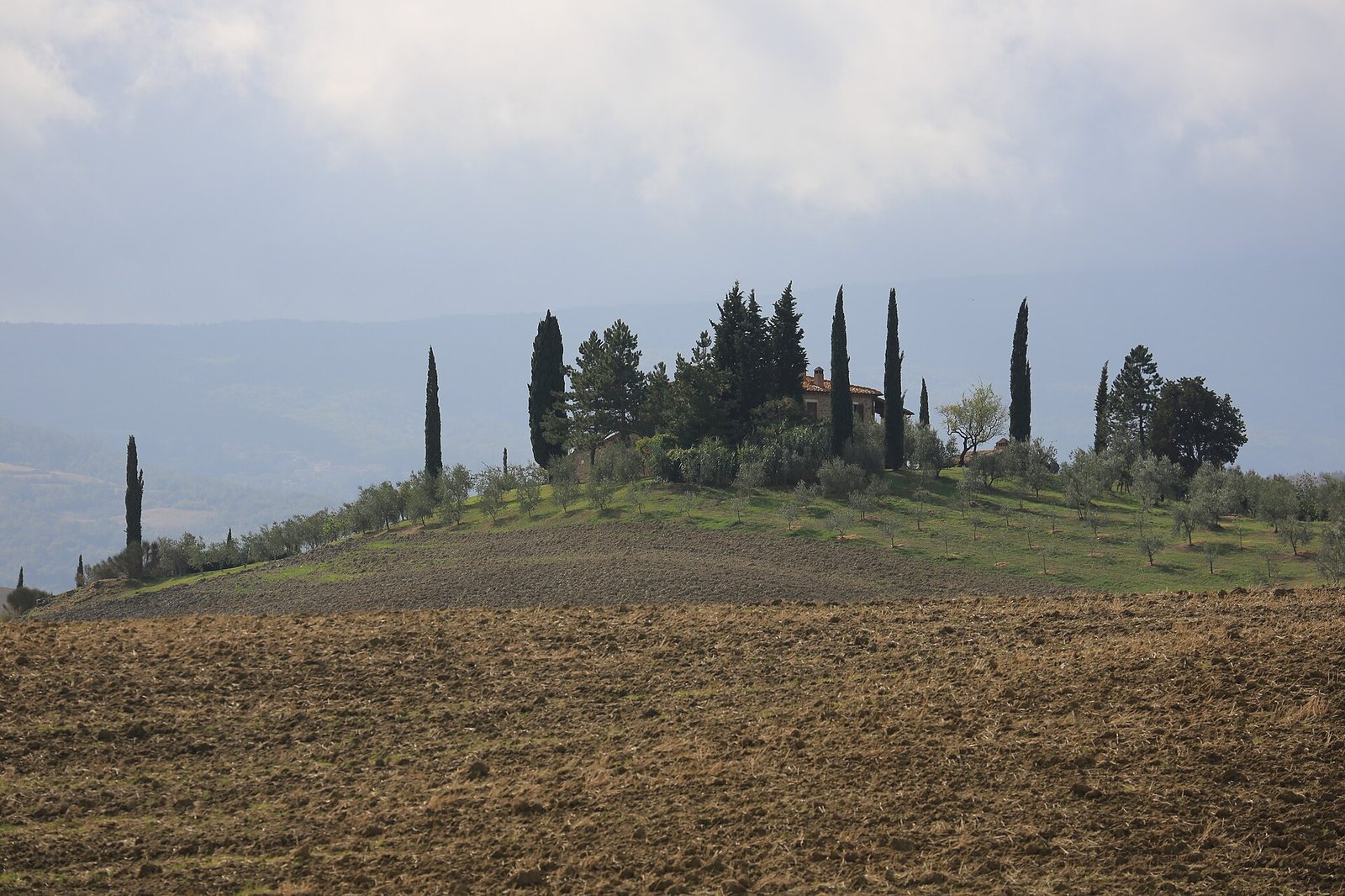 Light blue thermal pools are visible, bordered by white rock formations and a dirt path, with sparse vegetation on the banks under a cloudy sky.