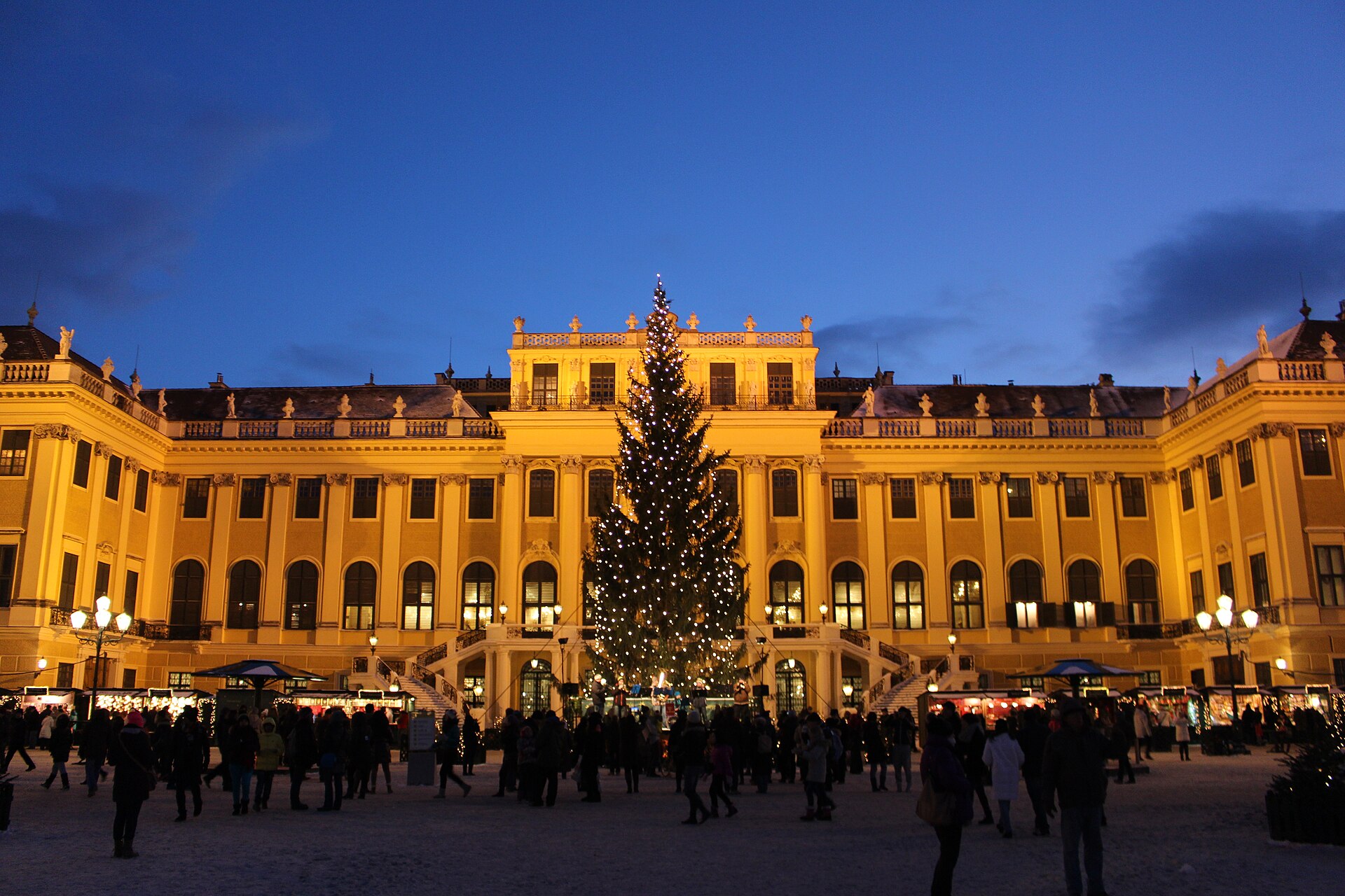 The yellow baroque facade of Schonbrunn Palace rises behind rows of wooden Christmas market stalls.