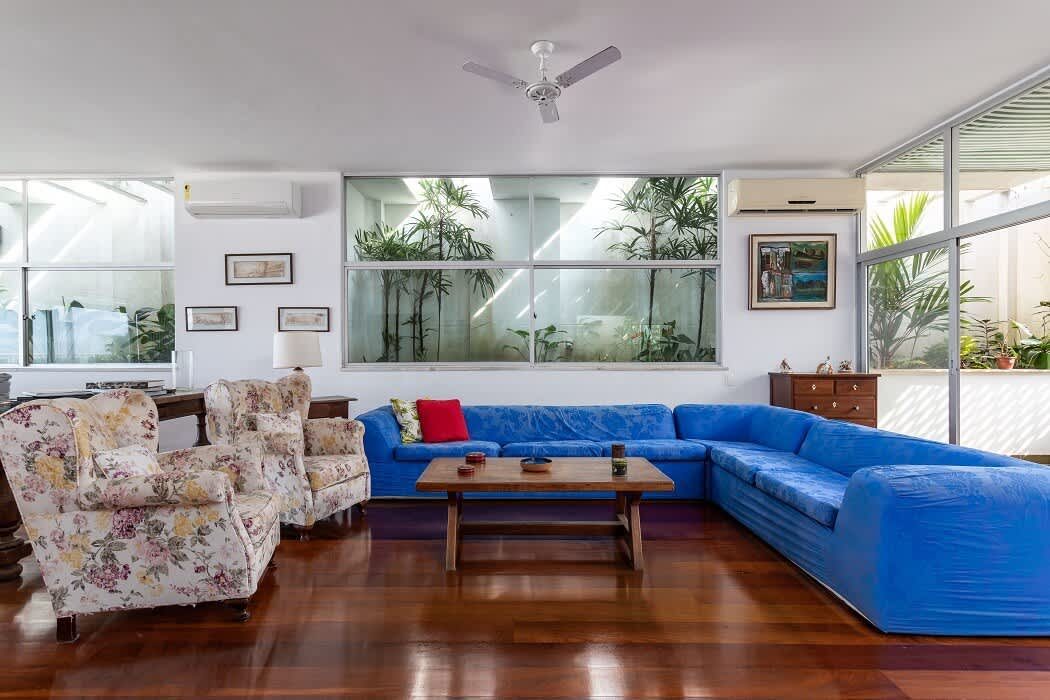 Living room with a blue sectional sofa, floral wing chairs and floor-to-ceiling garden windows