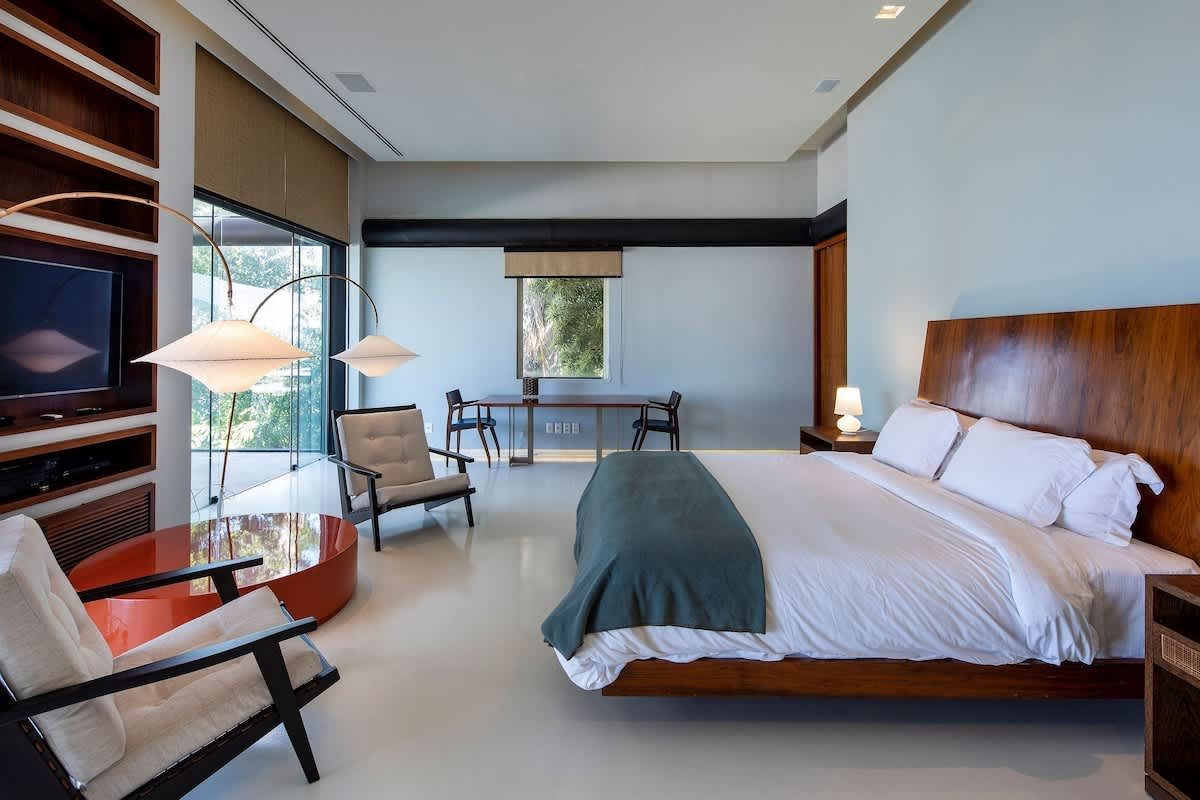 Bedroom suite with a dark wood headboard, king bed, and glass doors opening onto greenery at the São Conrado Beach View Villa