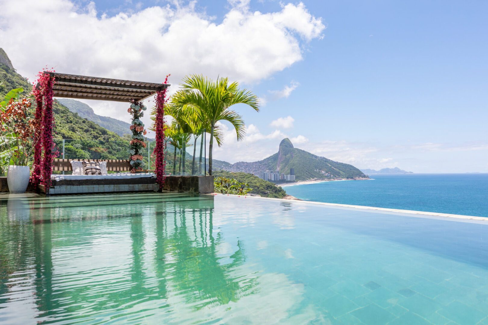 Infinity pool with a flower-draped daybed pergola at the São Conrado Beach View Villa, looking toward Pedra da Gávea and the Atlantic
