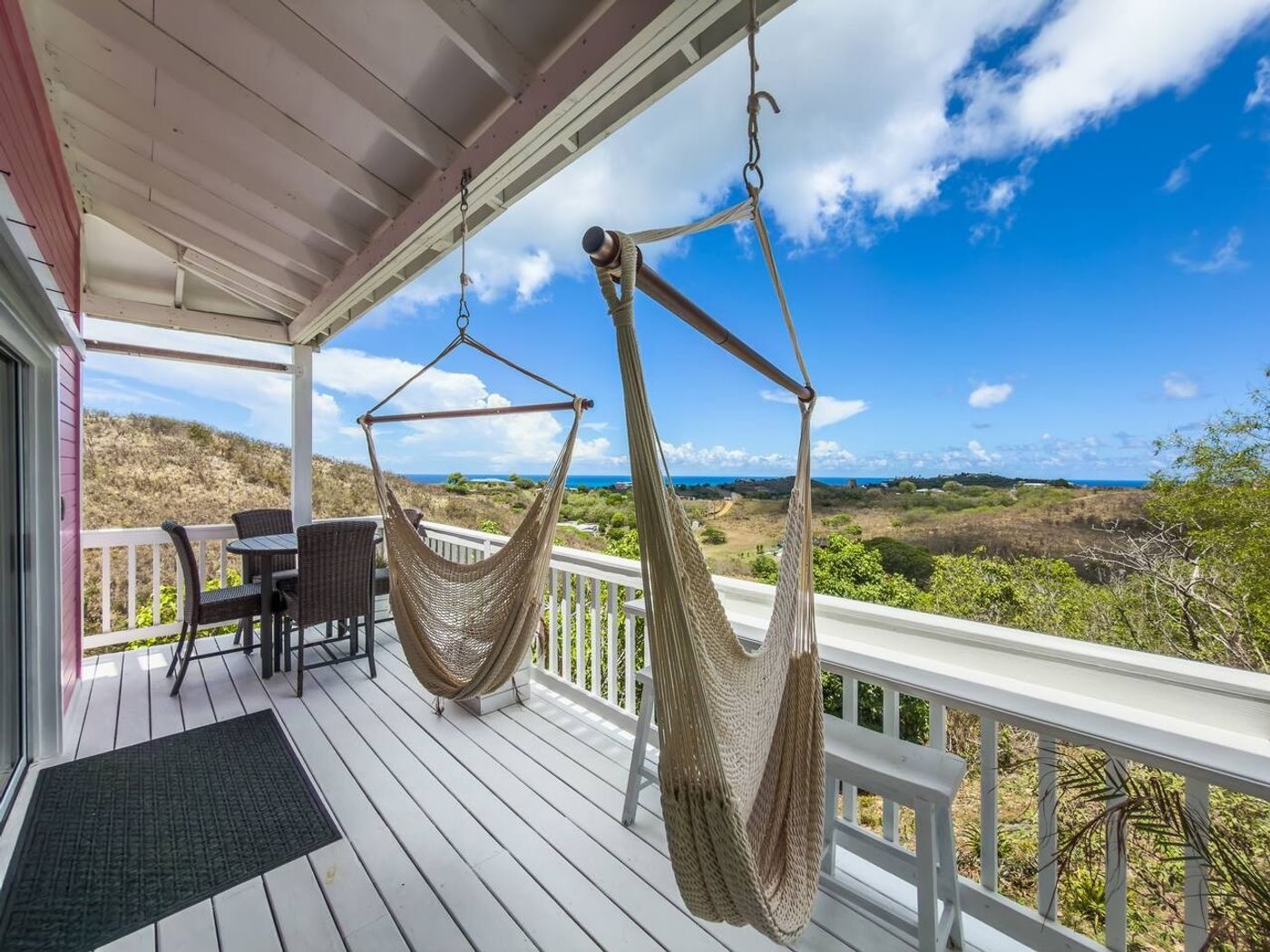 Covered porch with two hanging hammock chairs and a small dining table, looking over dry hills to the sea