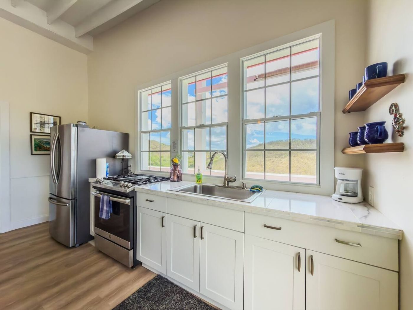 White kitchen with a gas range, a farmhouse sink under three windows and blue pottery on open shelves