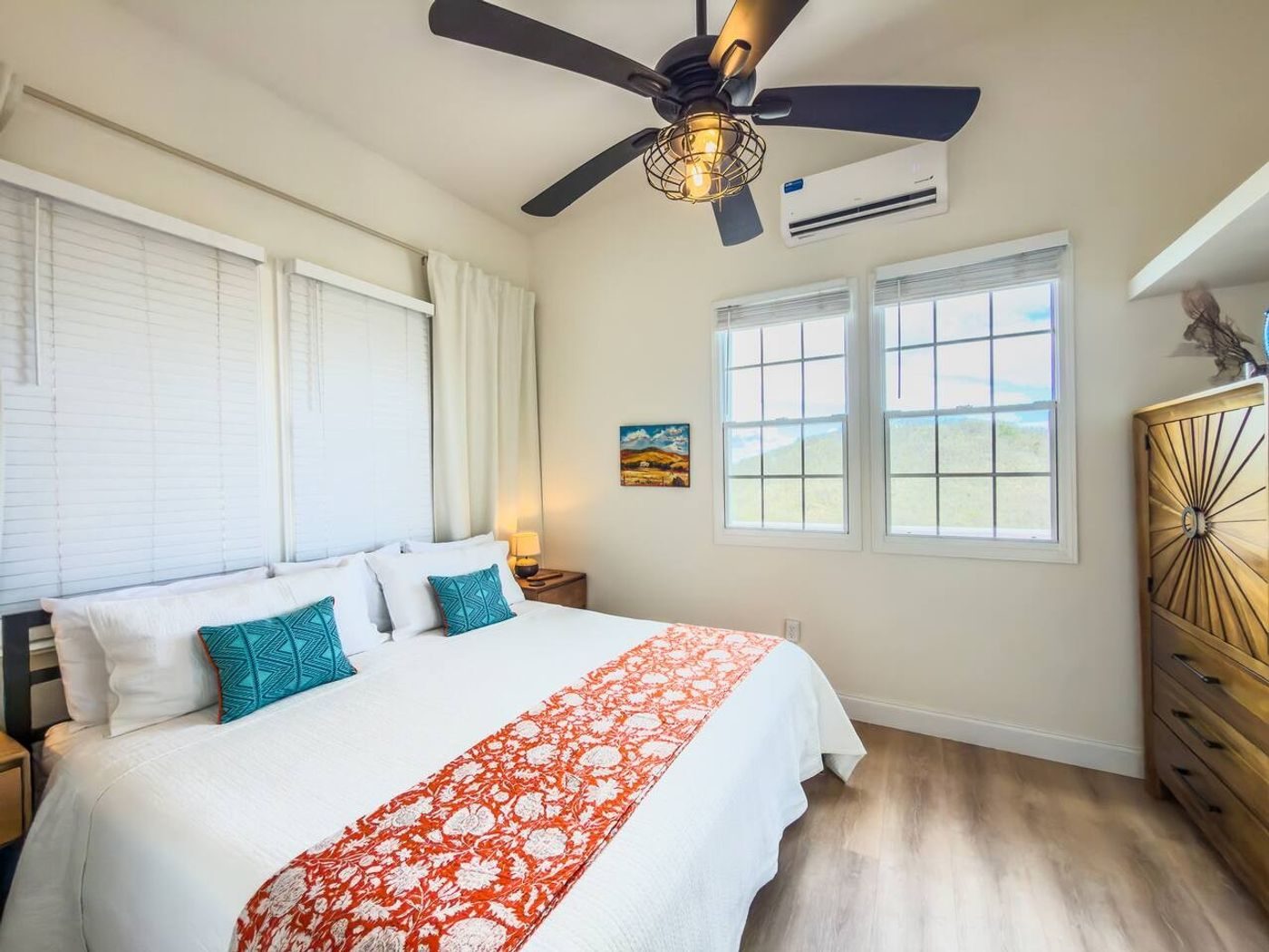 Bedroom with a king bed, a red and white throw and teal cushions under a ceiling fan