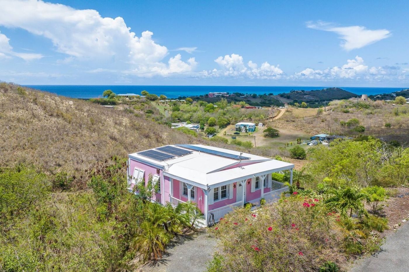 The pink cottage with solar panels on its roof, seen from above on a scrubby hillside with the sea beyond