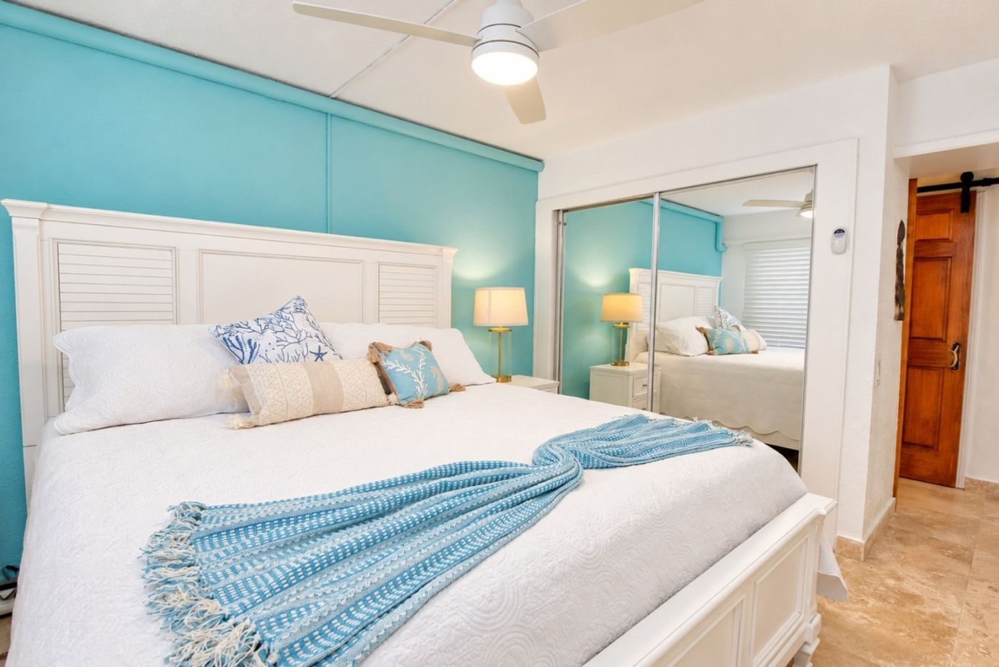 Bedroom with a king bed under a white headboard, a blue throw and a turquoise accent wall