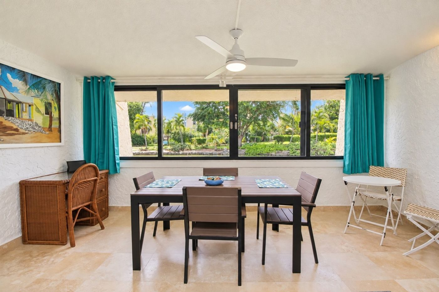 Dining table by a long window of green louvred frames looking onto palms and garden