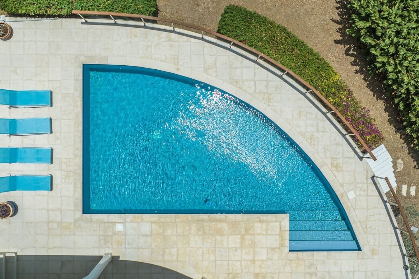 Overhead view of a quarter-circle pool with blue loungers along its curved stone edge