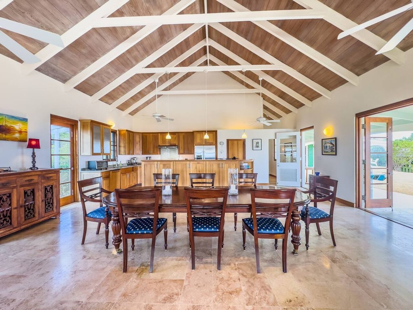 Long dining table under a pitched wood-lined ceiling with white beams, the kitchen beyond