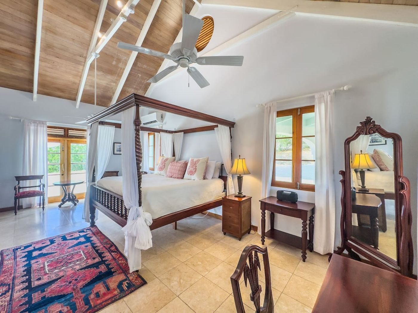 Bedroom with a dark four-poster bed hung with white netting, a patterned rug and a pitched wood ceiling