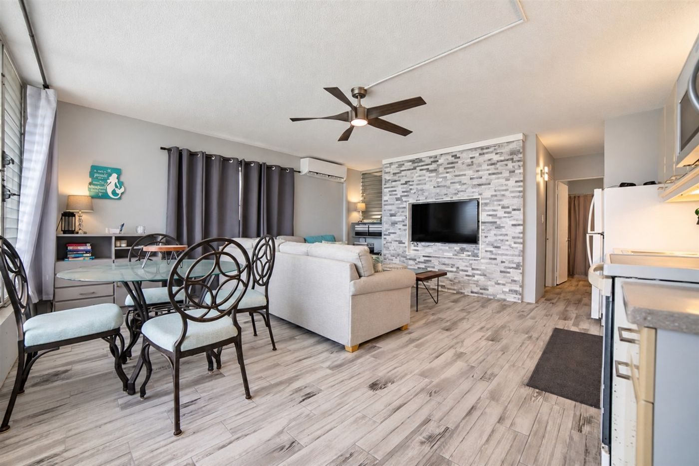 Living room with a grey sectional sofa, a stone accent wall with a television and a round glass dining table
