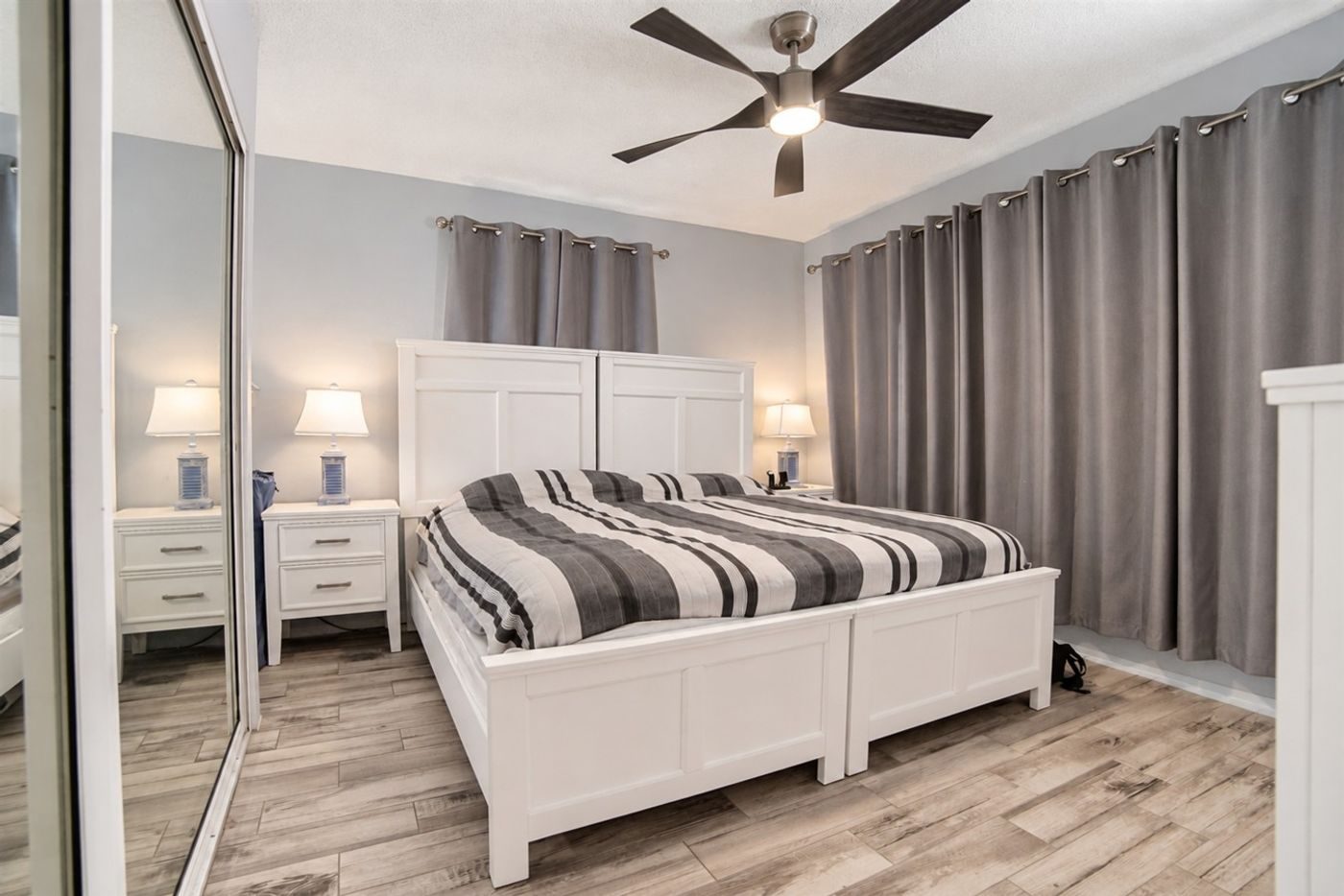 Bedroom with a king bed under a white headboard, a striped grey and white cover and grey curtains