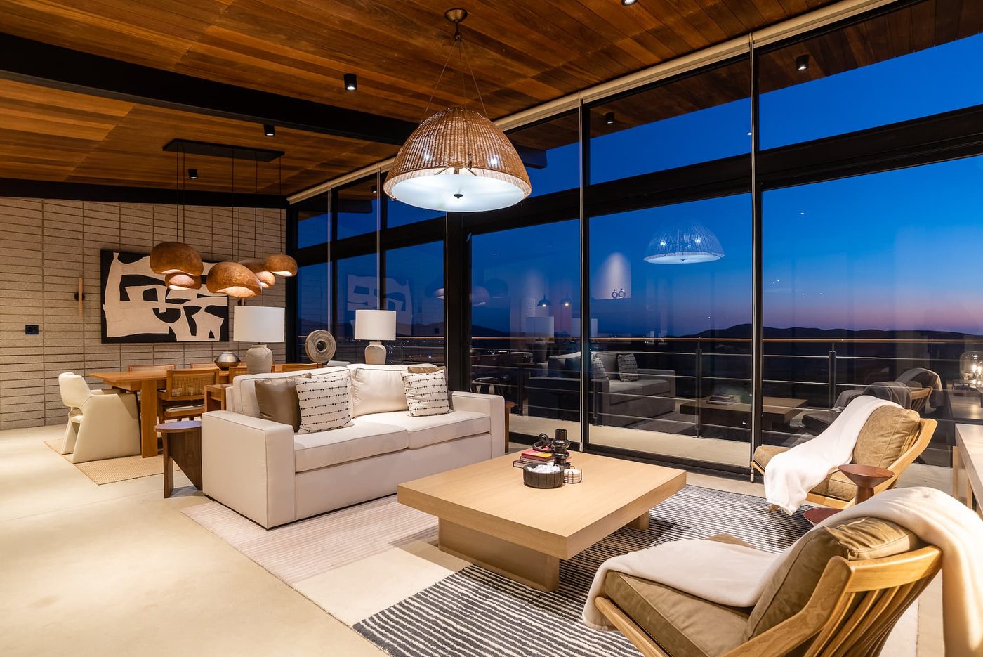 The great room at Casa Finch at dusk, glass walls on every side opening onto the valley