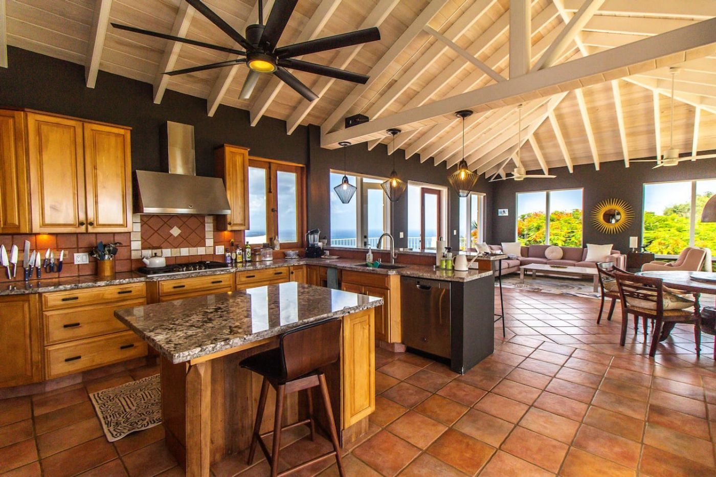 Kitchen with wood cabinets, a granite island and terracotta floor tiles under a high white beamed ceiling