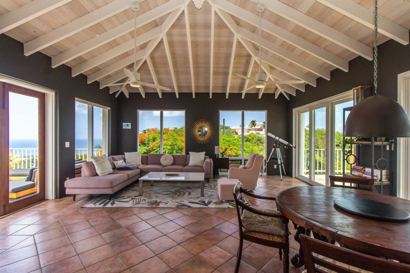 Open living and dining room with a pink sofa, a round wooden table and windows on every side