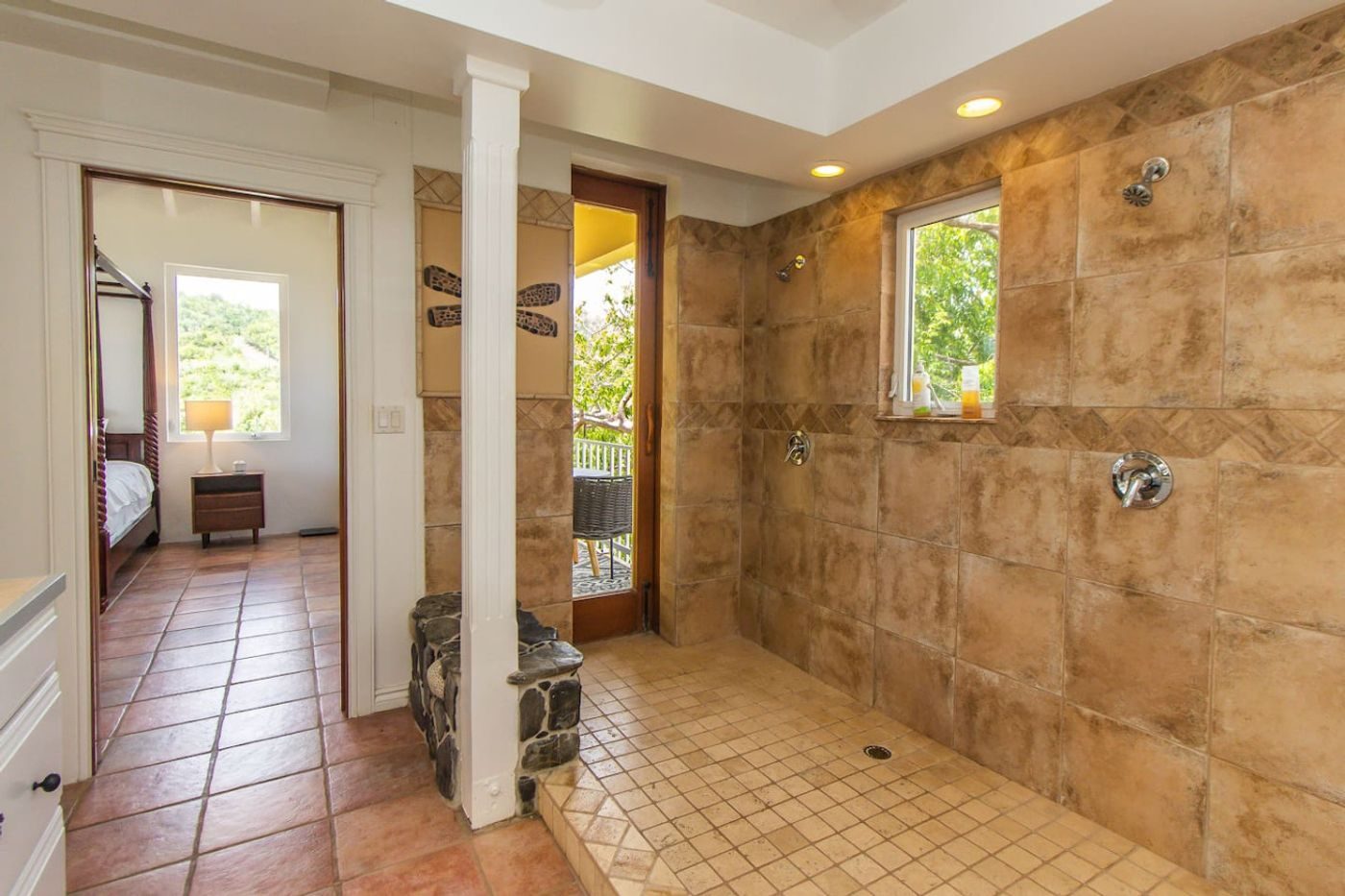 Large open walk-in shower lined with stone-coloured tile, with a window onto greenery