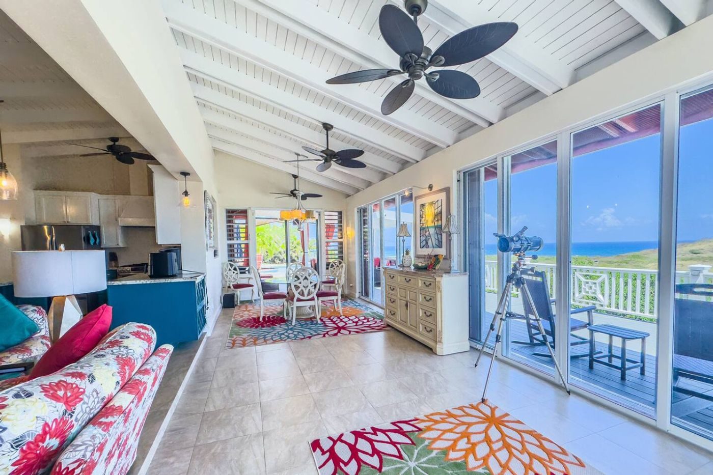 Bright living room with a white beamed ceiling, colourful floral sofas and sliding glass doors to the balcony, a telescope by the window