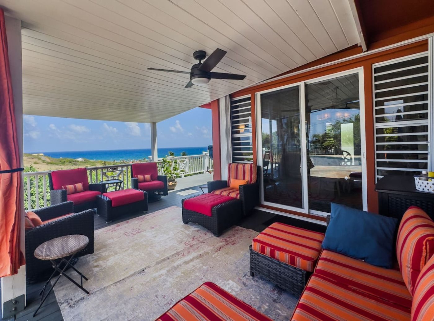 Covered porch with red and orange striped outdoor sofas and armchairs, the sea beyond the railing
