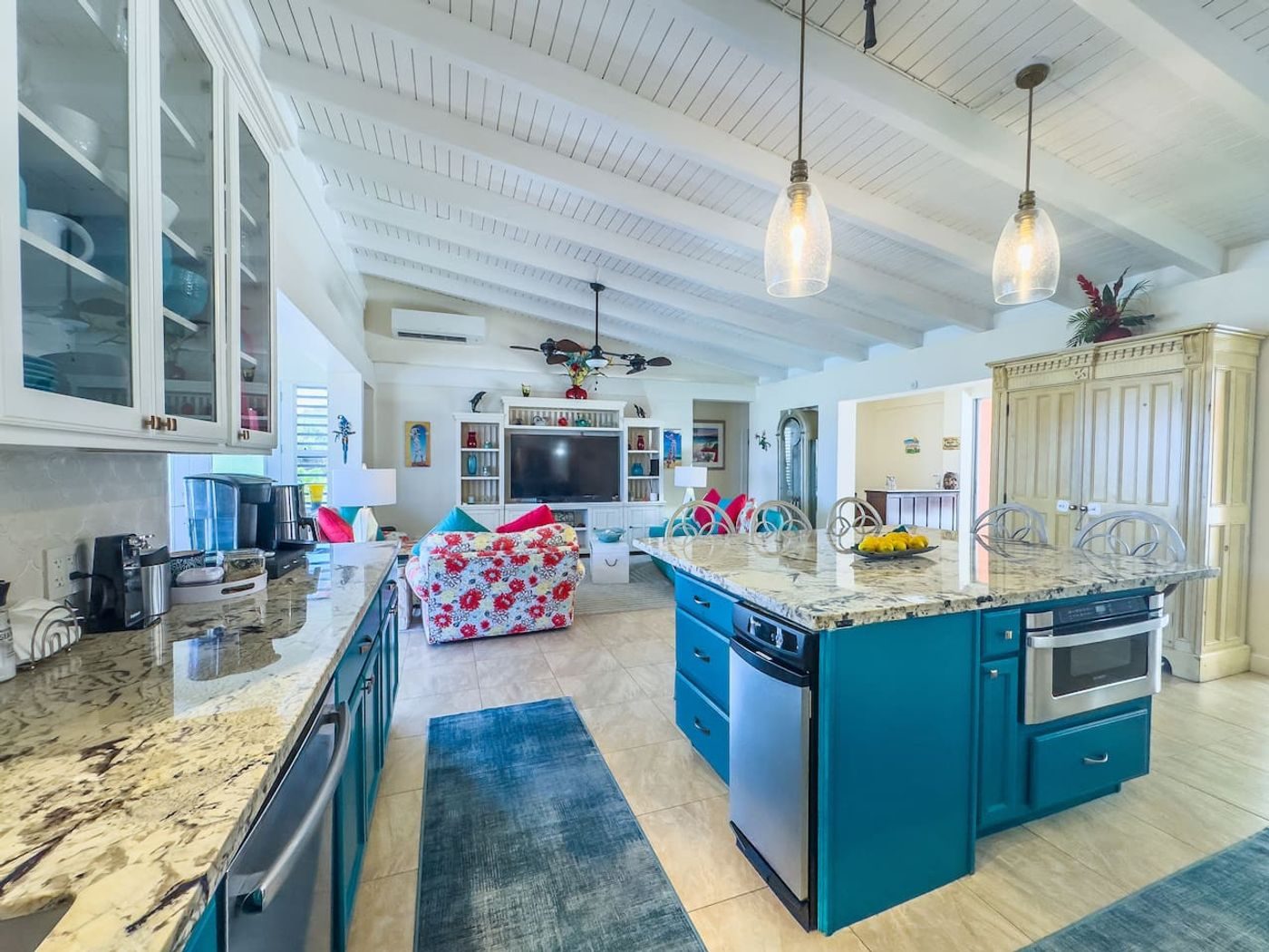 Kitchen with a teal island, granite counters, stainless steel appliances and pendant lights under a white beamed ceiling