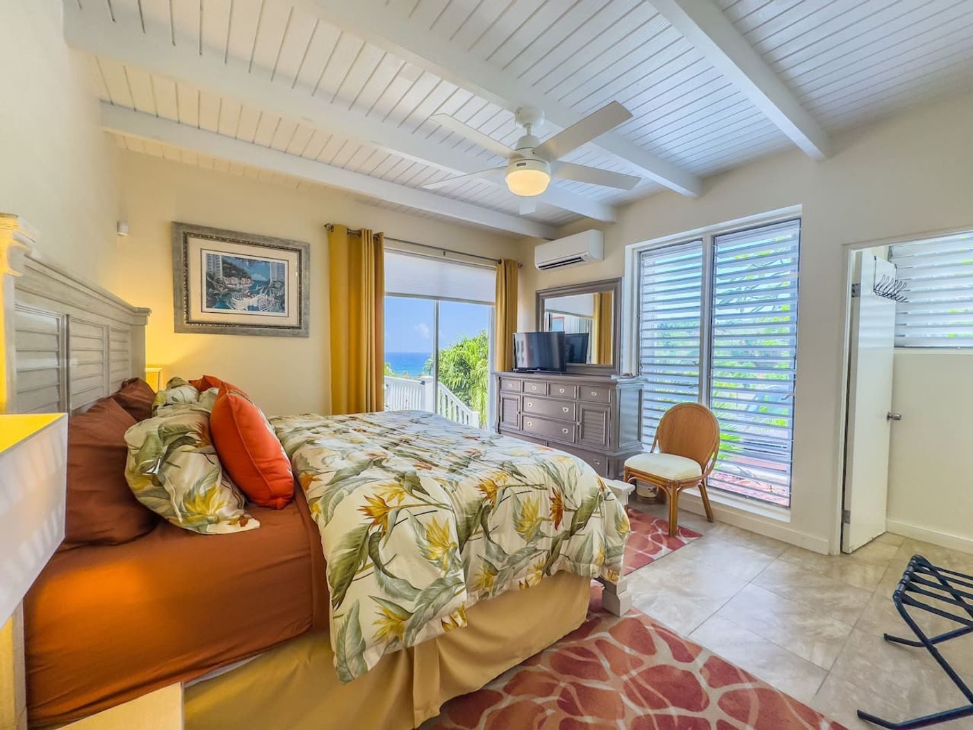 Bedroom with a tropical-print bedspread, orange cushions and a window onto the sea