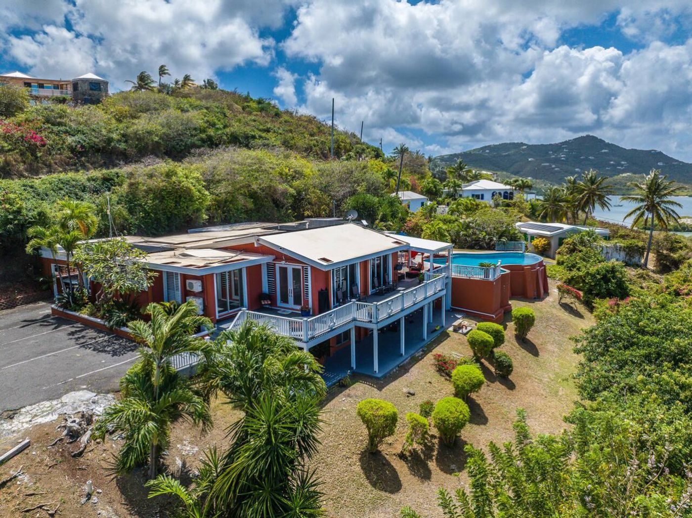 Aerial view of the burnt-orange villa with white railings, its pool and gardens on a green hillside