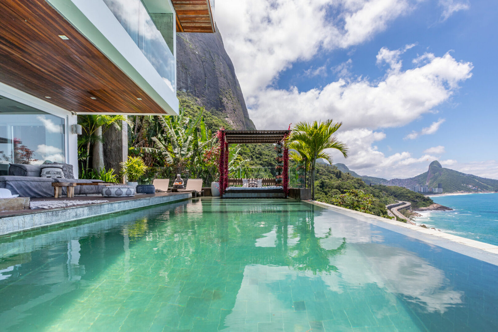 Infinity pool and a shaded daybed cabana on the cliff at Joá, with the Rio de Janeiro coastline beyond