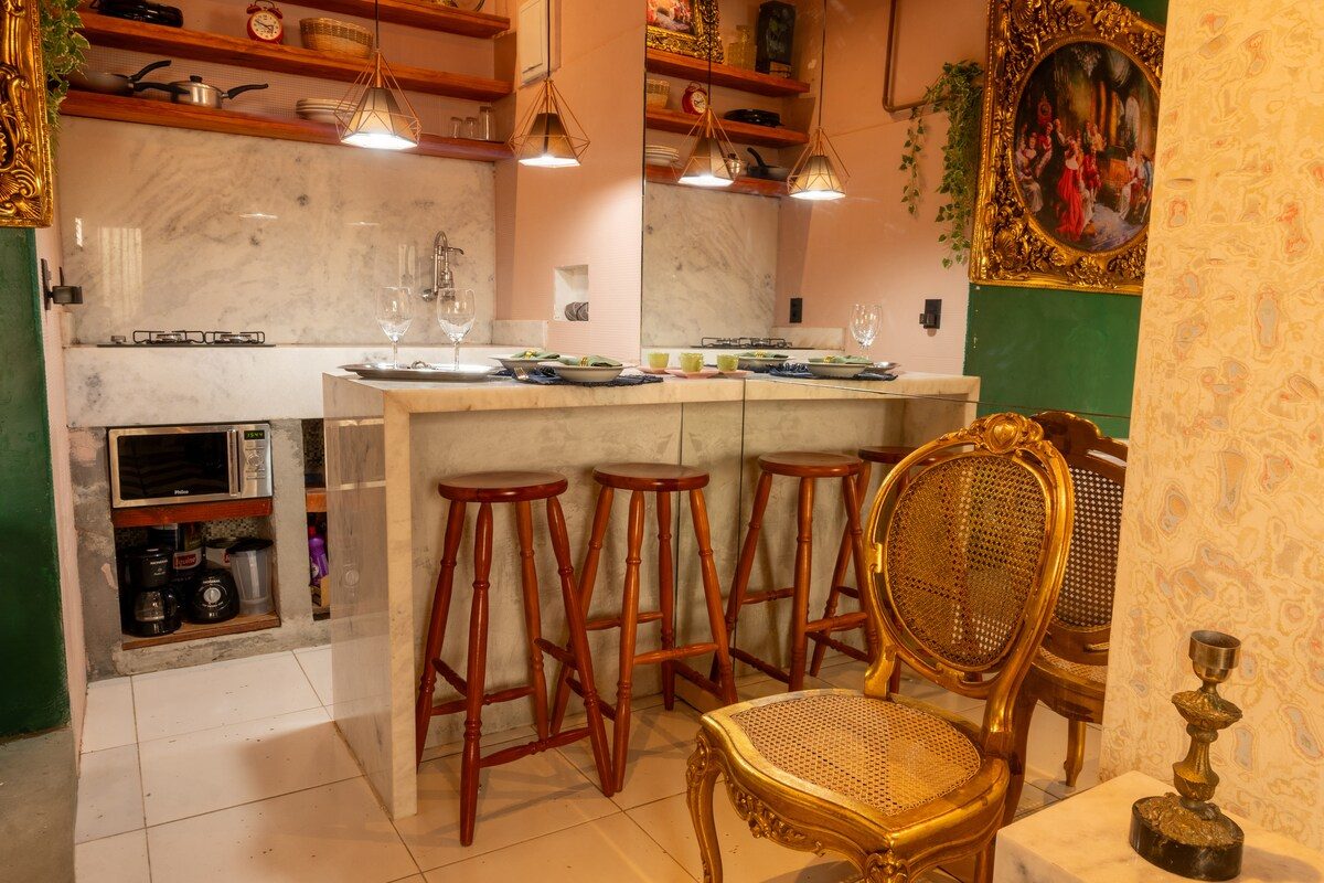 Kitchen bar with three wooden stools, a gilt chair, shelves of copper pans and pendant lamps