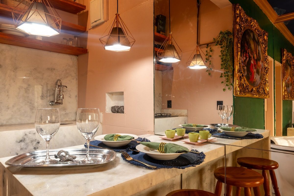 Marble counter with two wine glasses, plates and a tray, pendant lights and a framed painting