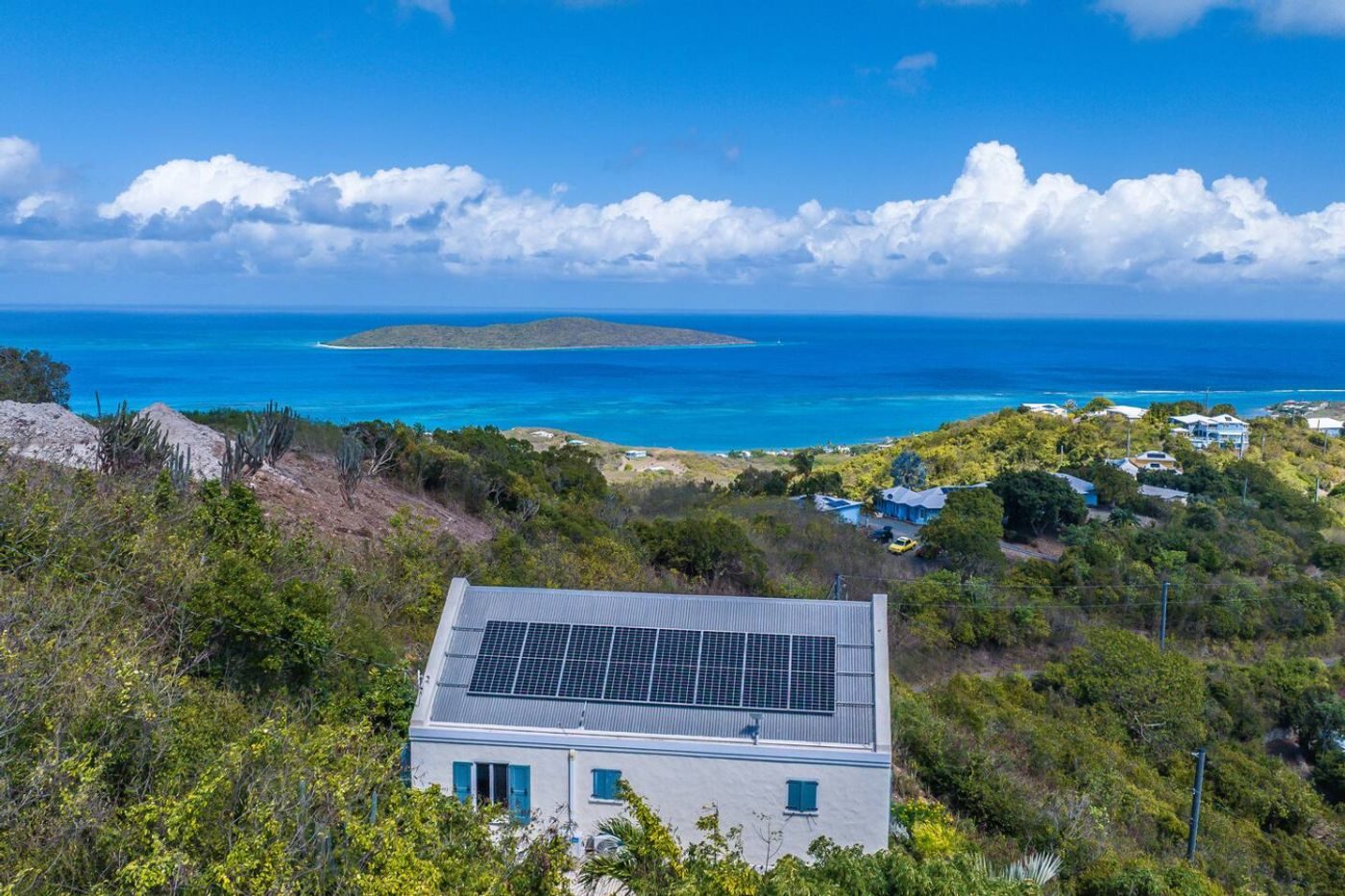 View over the house's solar-panelled roof and green hills to a turquoise sea and Buck Island