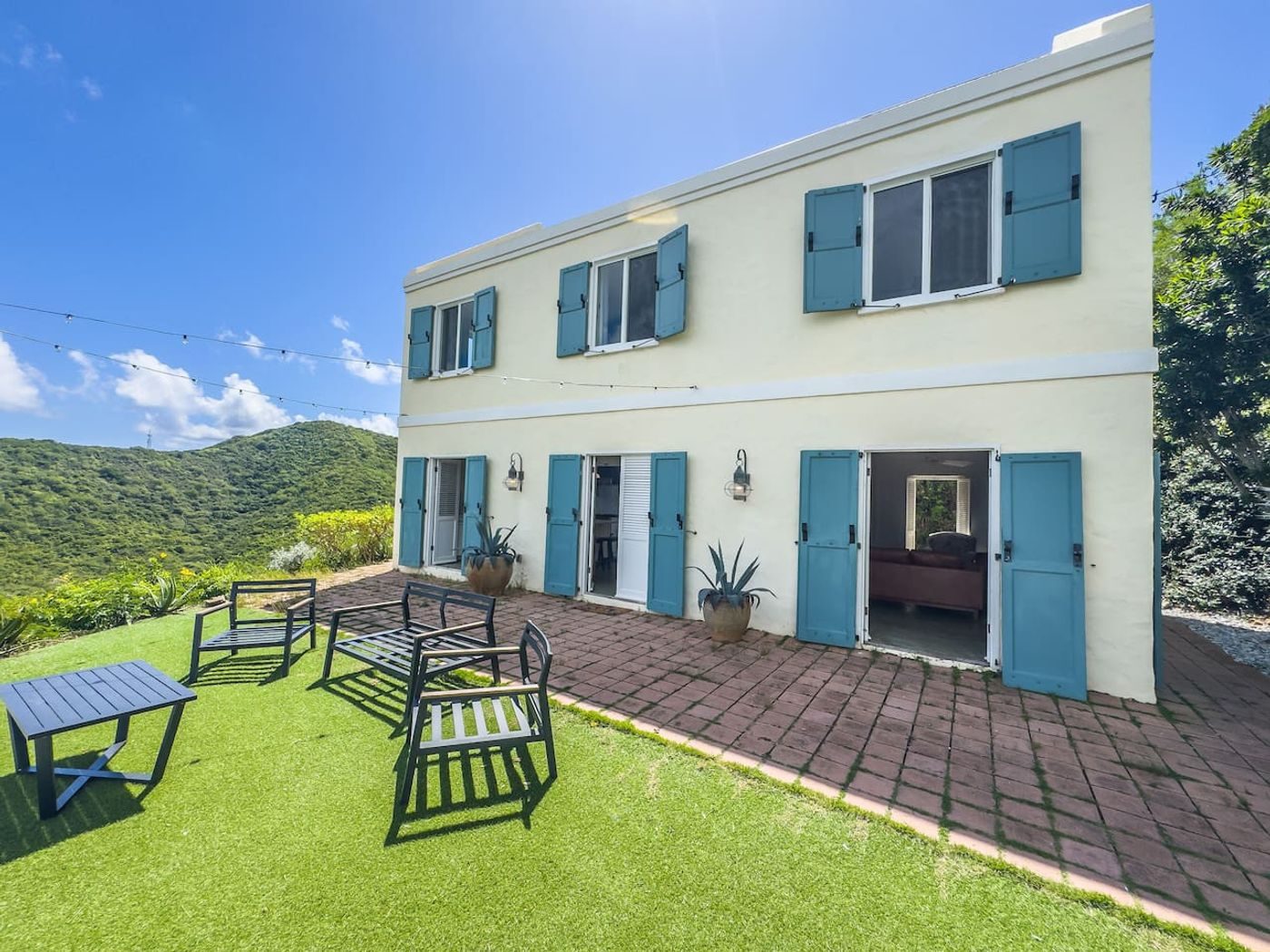 Brick patio and lawn with outdoor chairs in front of the white house with blue shutters
