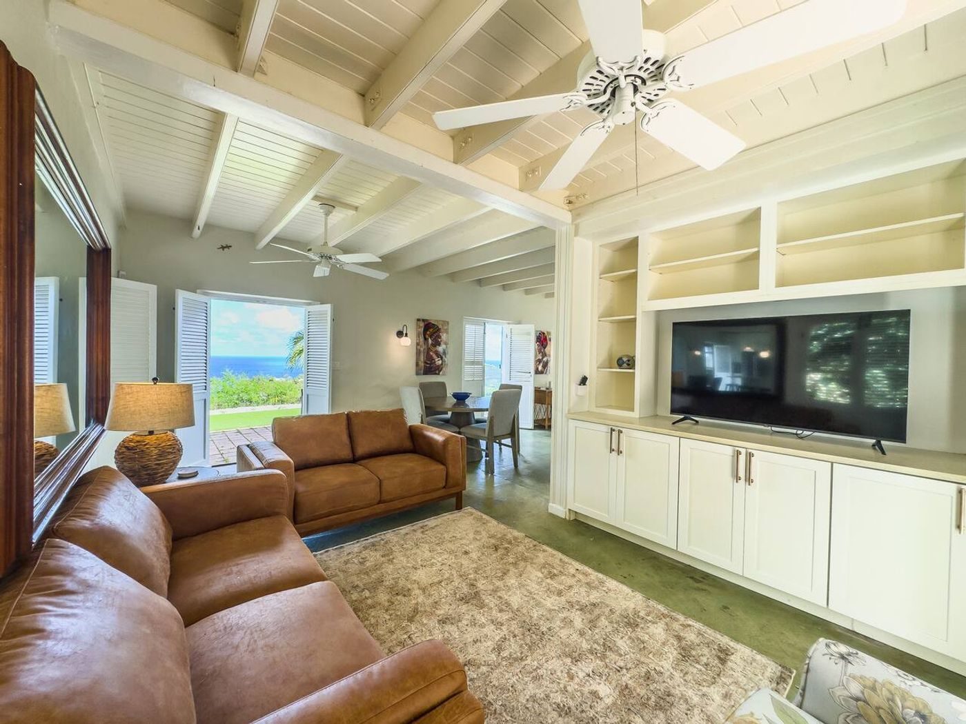 Living room with a tan leather sofa, built-in white shelving and a television, under a white beamed ceiling