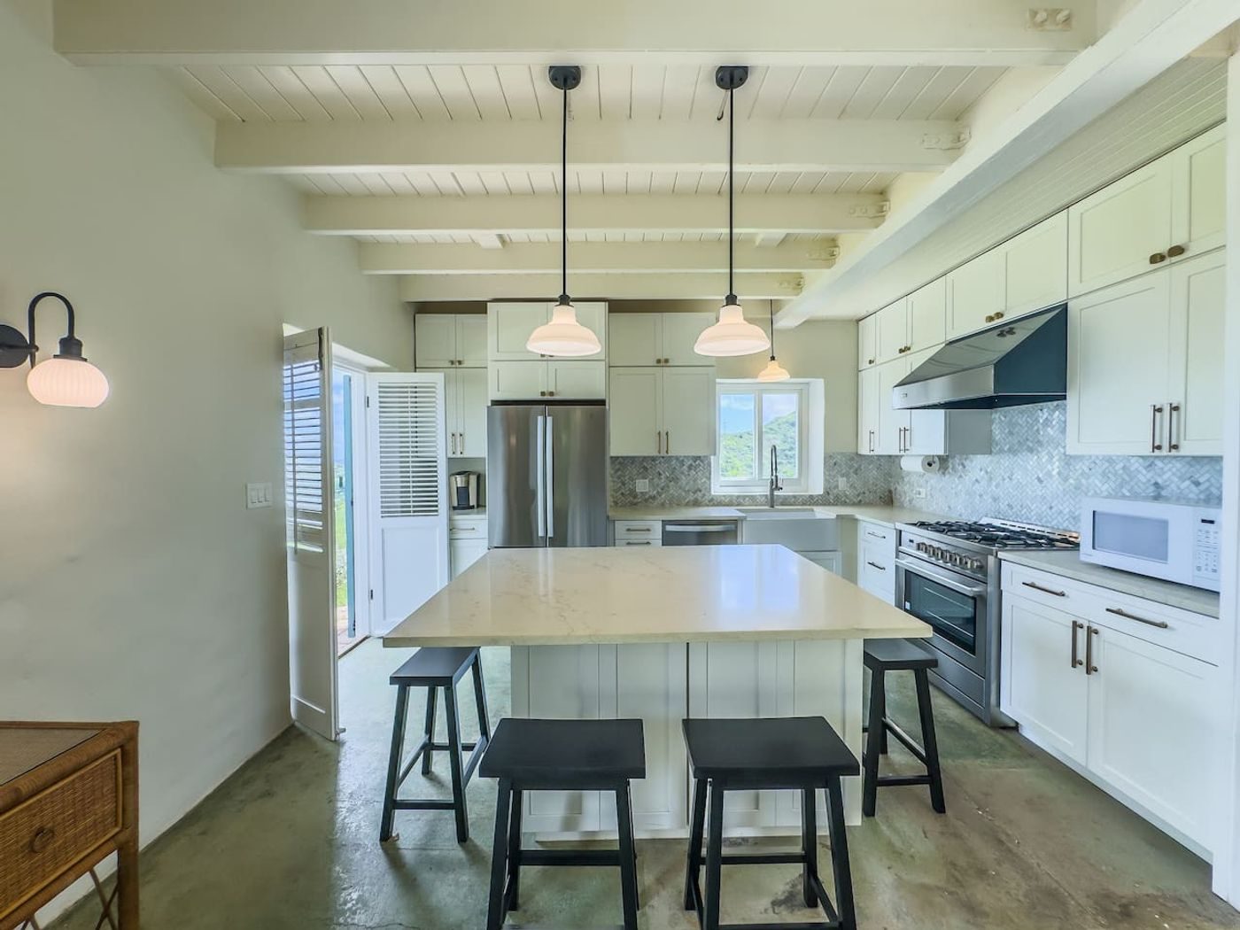 White kitchen with an island, black stools, pendant lights and stainless steel appliances