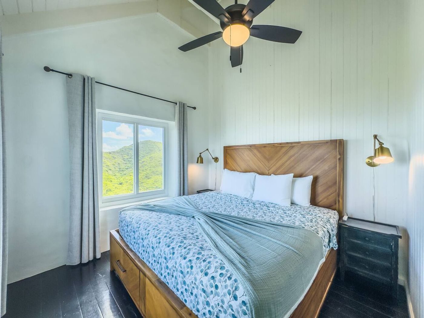 Bedroom with a wood headboard, a blue patterned quilt and a window onto green hills