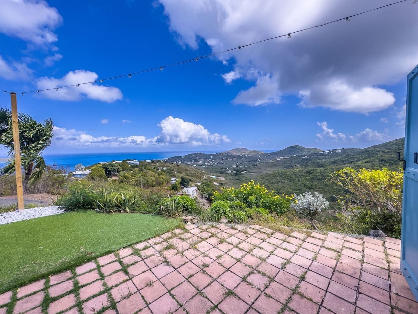 Brick patio at the edge of the lawn looking down over green hills to the sea