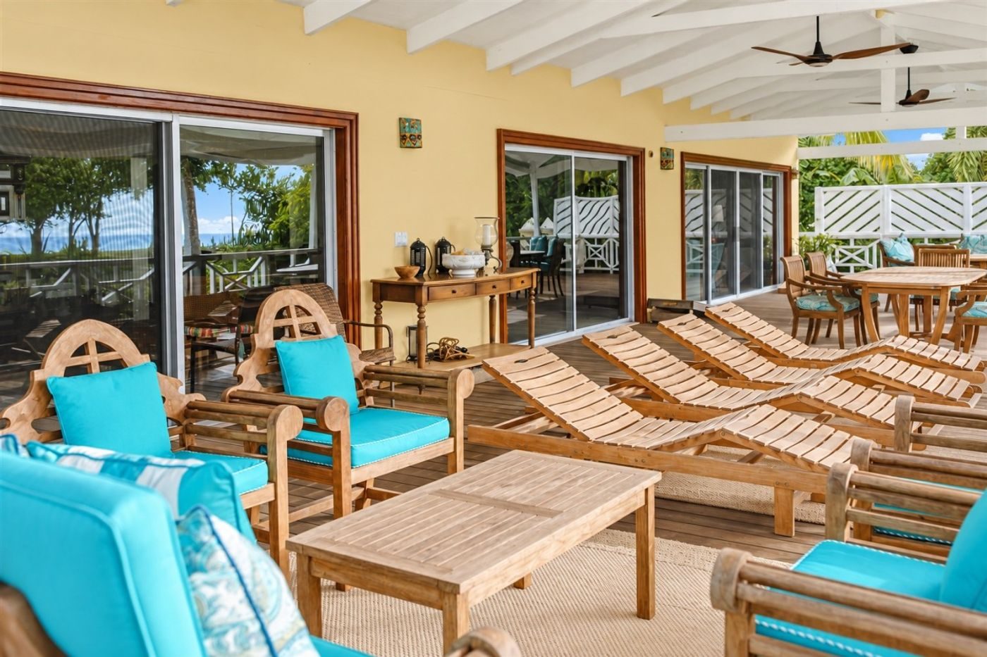 Covered gallery with teak loungers and armchairs with turquoise cushions