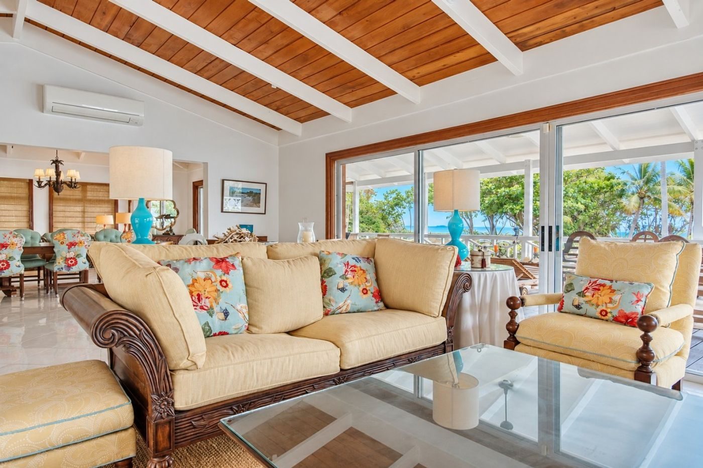Living room with cream sofas, a glass coffee table and sliding doors, under a wood-lined ceiling with white beams