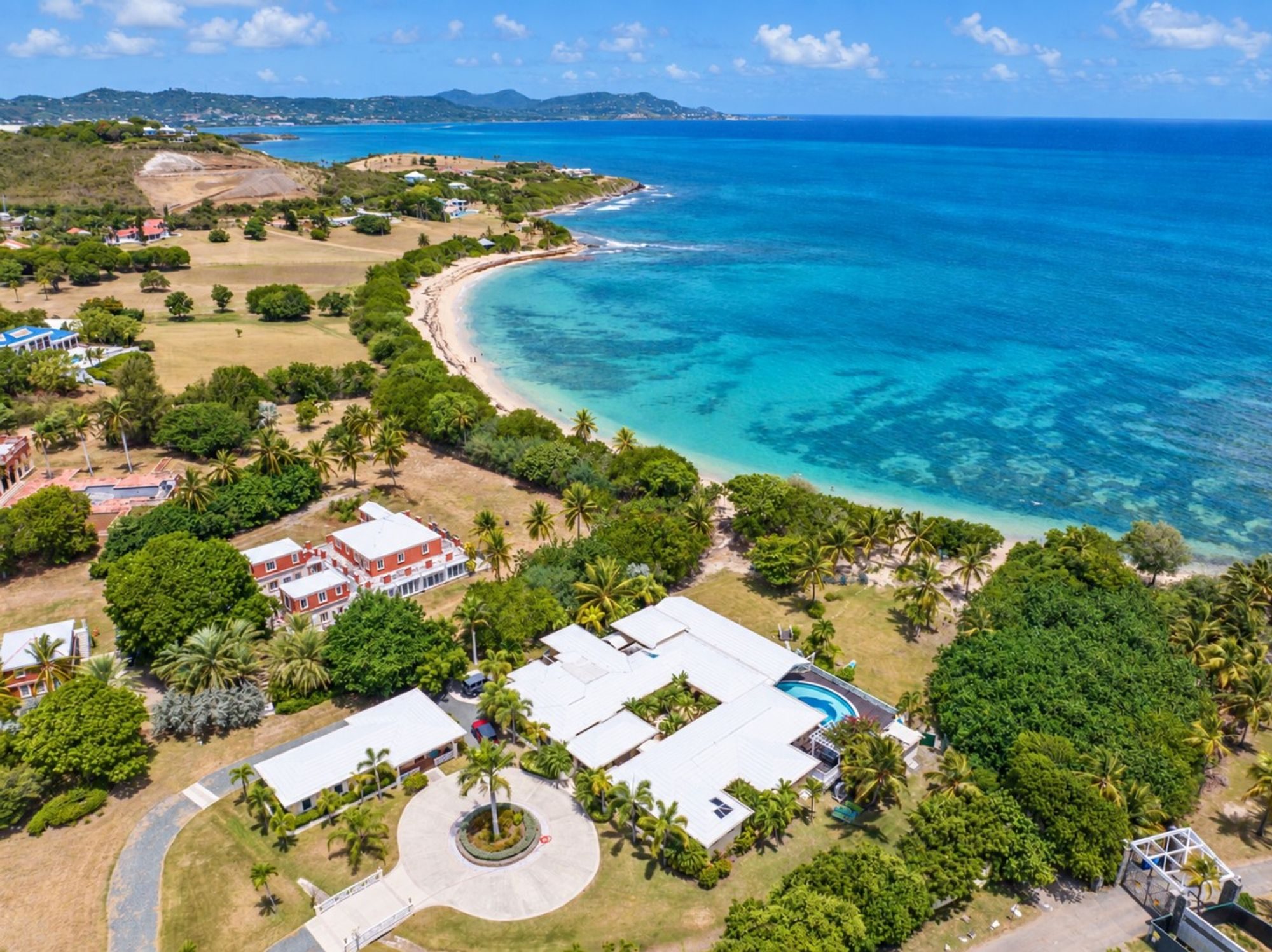 Aerial view of a white-roofed villa among trees beside a long curving bay of turquoise water on St. Croix