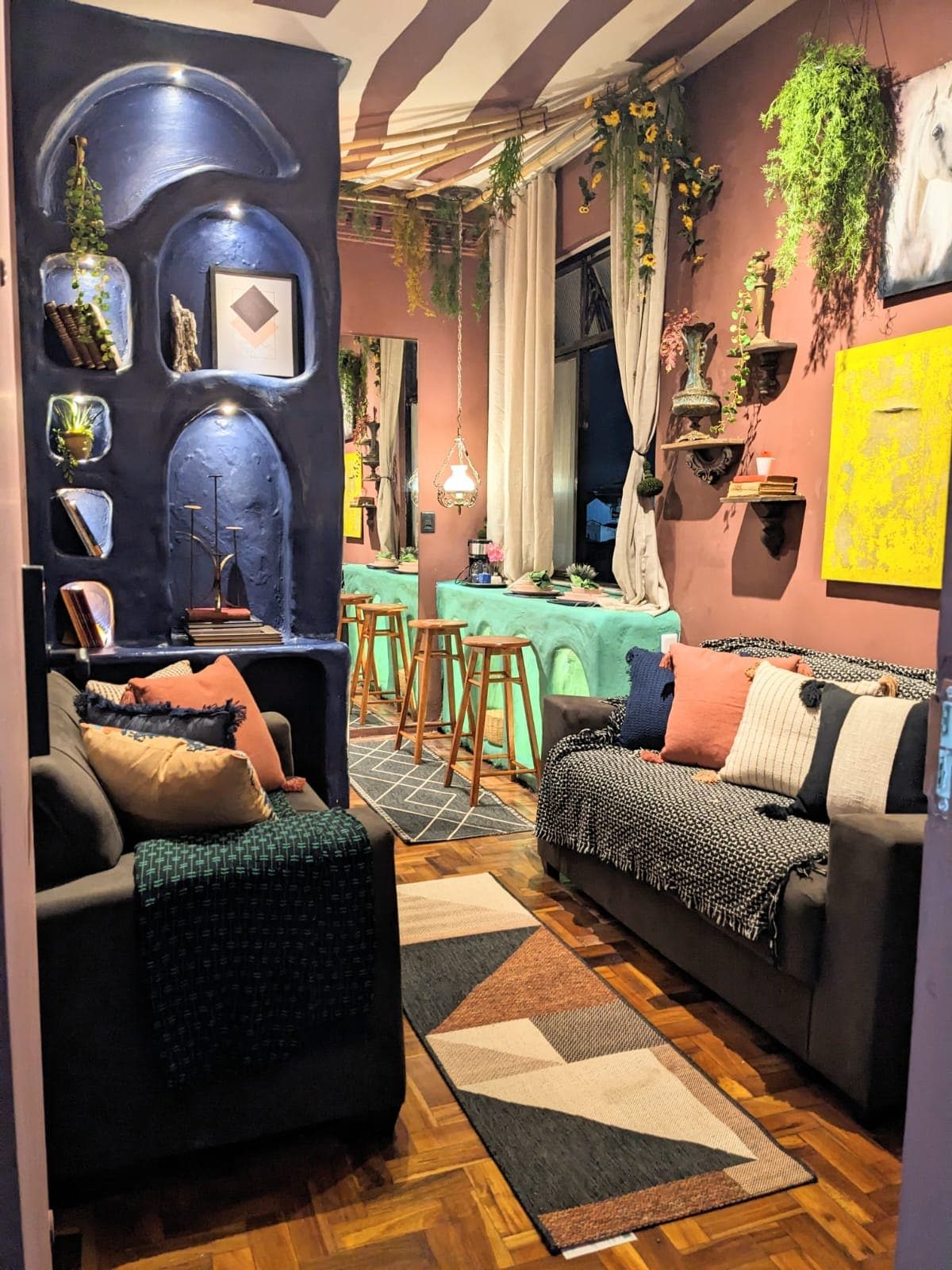 Living room with plum walls, blue arched niches holding ceramics, two dark sofas with patterned cushions and a geometric rug