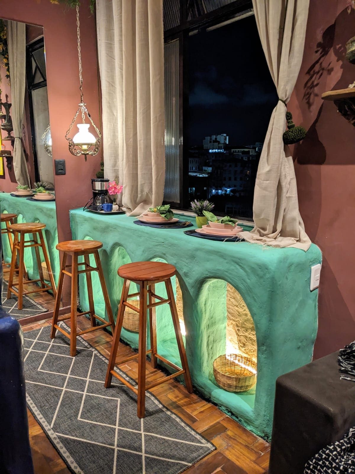 Mint-green bar counter with wooden stools along a window, the city lights outside at night
