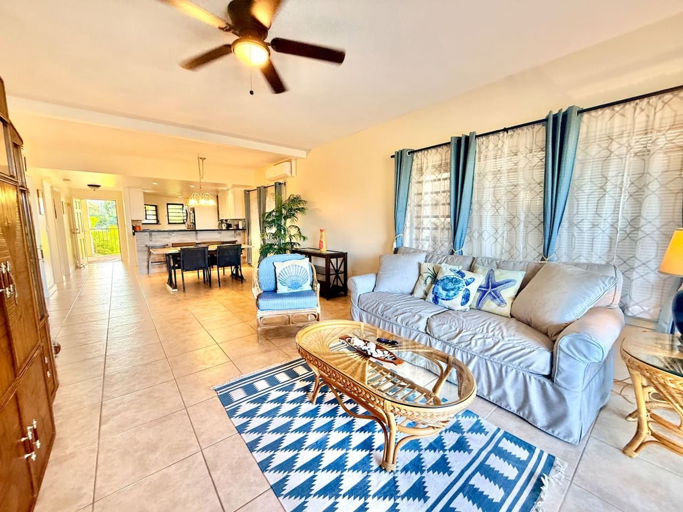 Bright living room with white slipcovered sofas, a blue patterned rug, a rattan coffee table and a dining area beyond