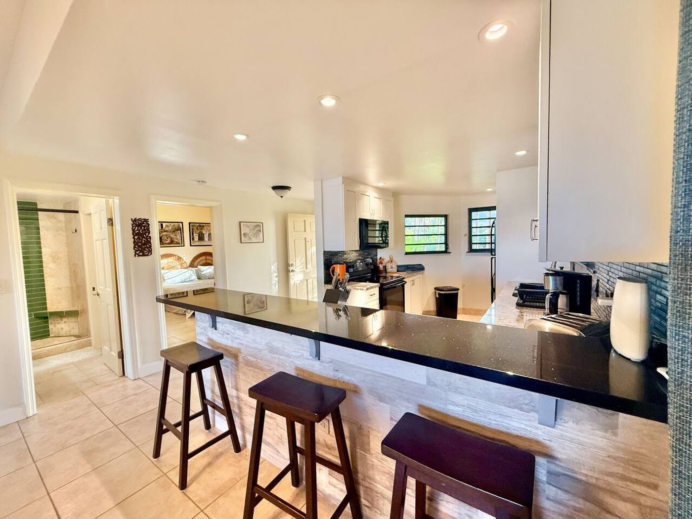 Kitchen bar with a black granite counter and three wooden stools, white cabinets and a green glass tile splash