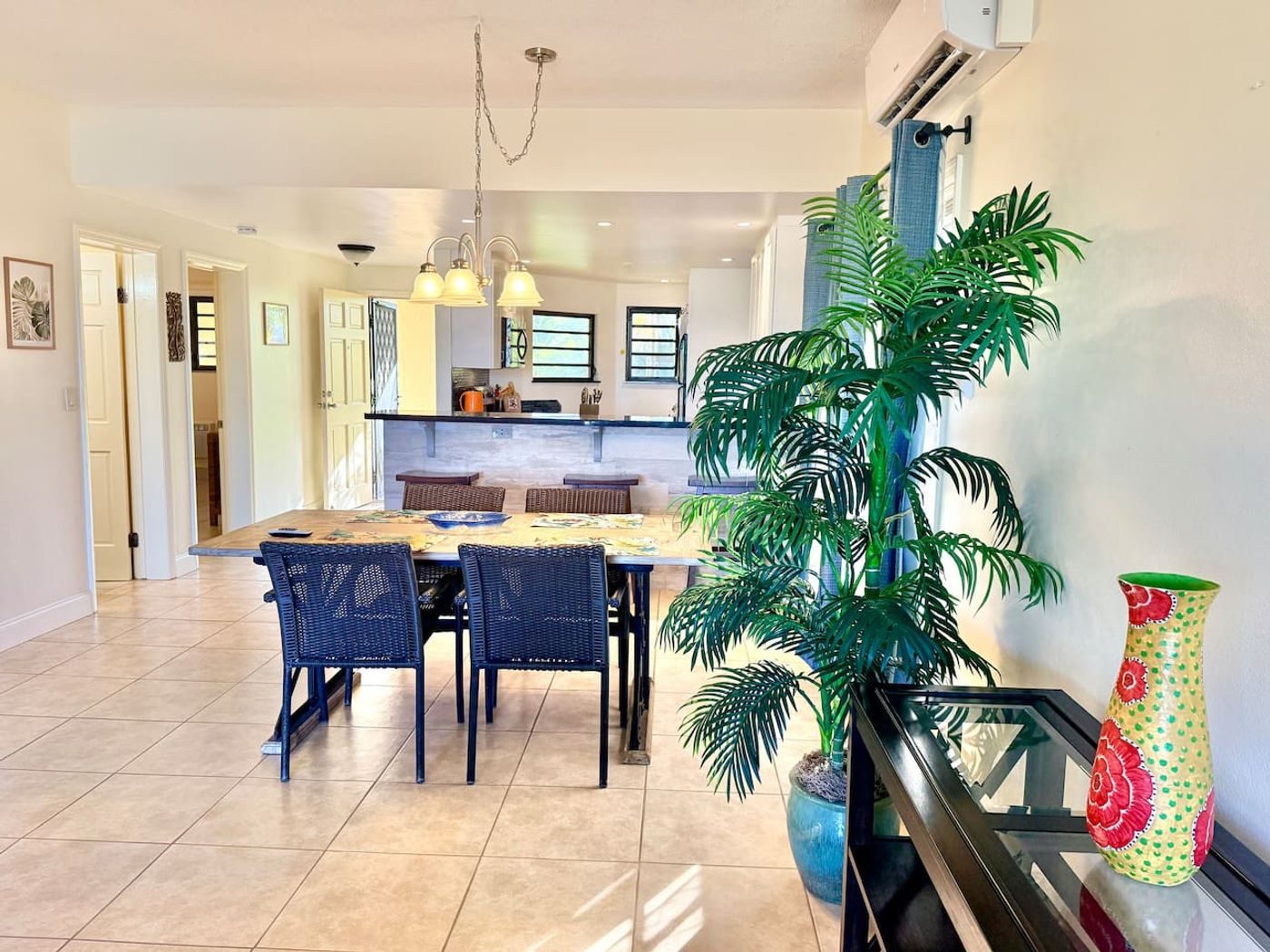 Open-plan dining area with a dark dining table, a tall potted palm and the kitchen behind