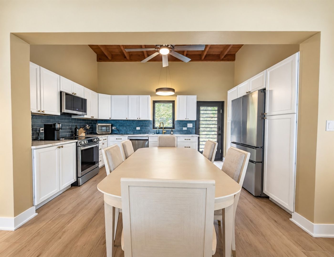 White kitchen with a blue tile backsplash, stainless steel appliances and a dining table under a wood ceiling