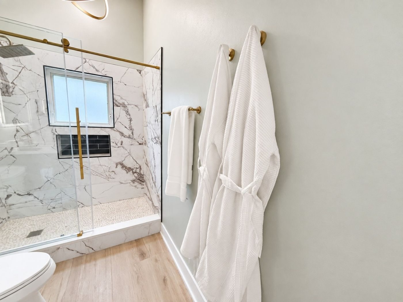 Bathroom with a marble-look walk-in shower, brass fittings and two white robes on hooks