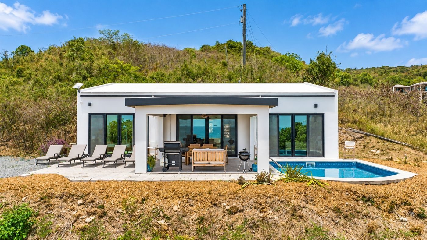 Modern single-storey white villa with black-framed glass doors, a covered terrace and a small pool on a dry scrub hillside