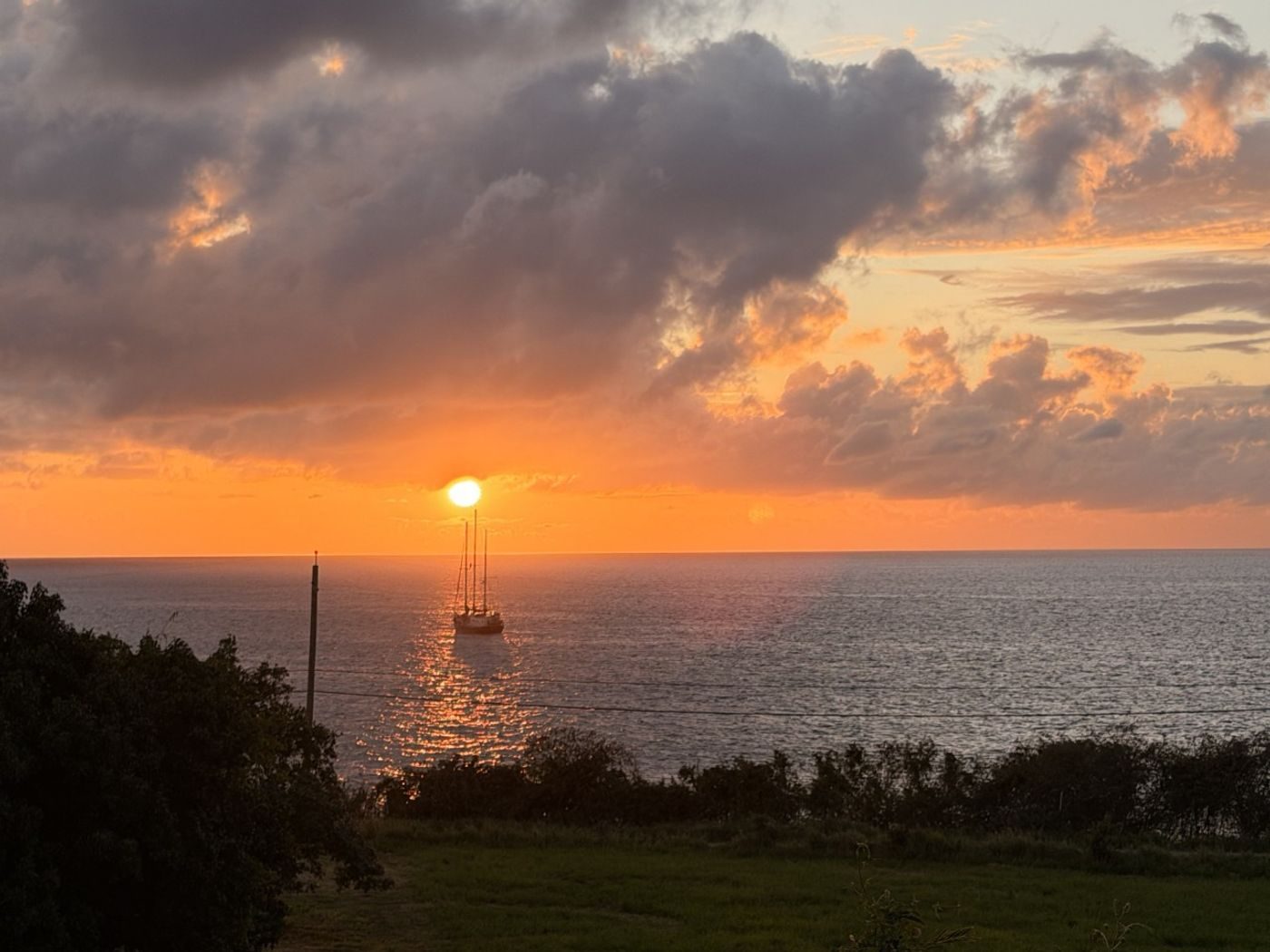The sun setting into the sea under orange clouds, a sailboat silhouetted offshore