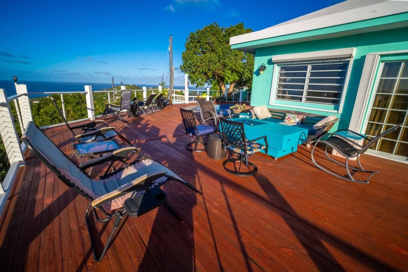 Upper deck with recliners, rocking chairs and a turquoise fire table beside the turquoise house