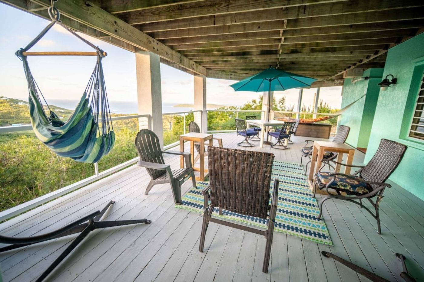 Covered lower deck with a hanging hammock chair, armchairs and an umbrella table looking over the trees