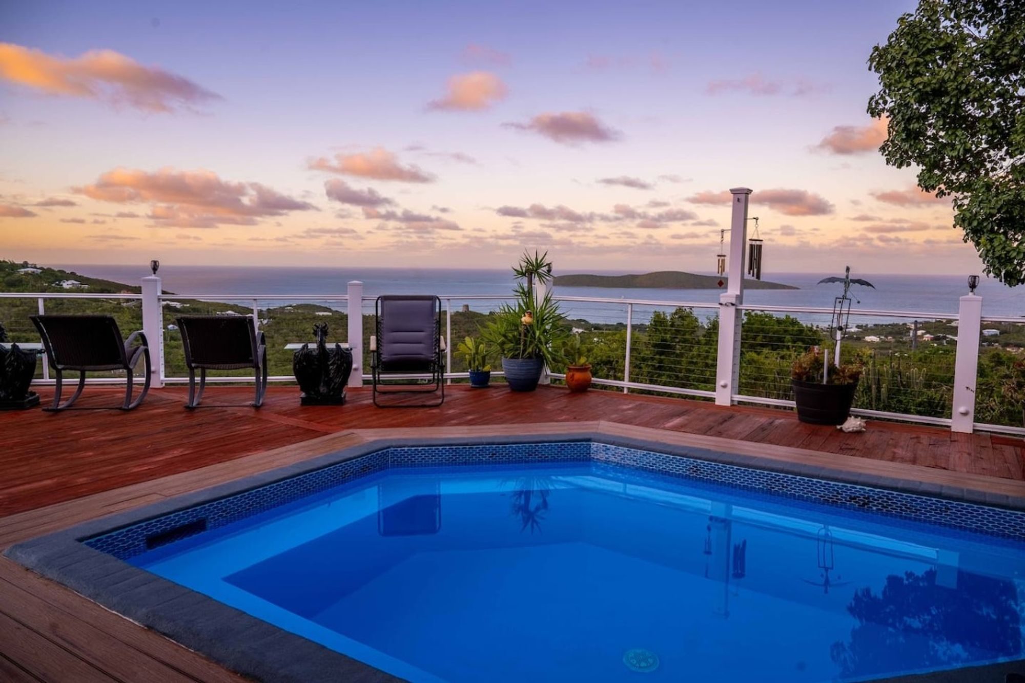 Private pool on a red wooden deck at sunset, with a white railing and the sea and an island beyond